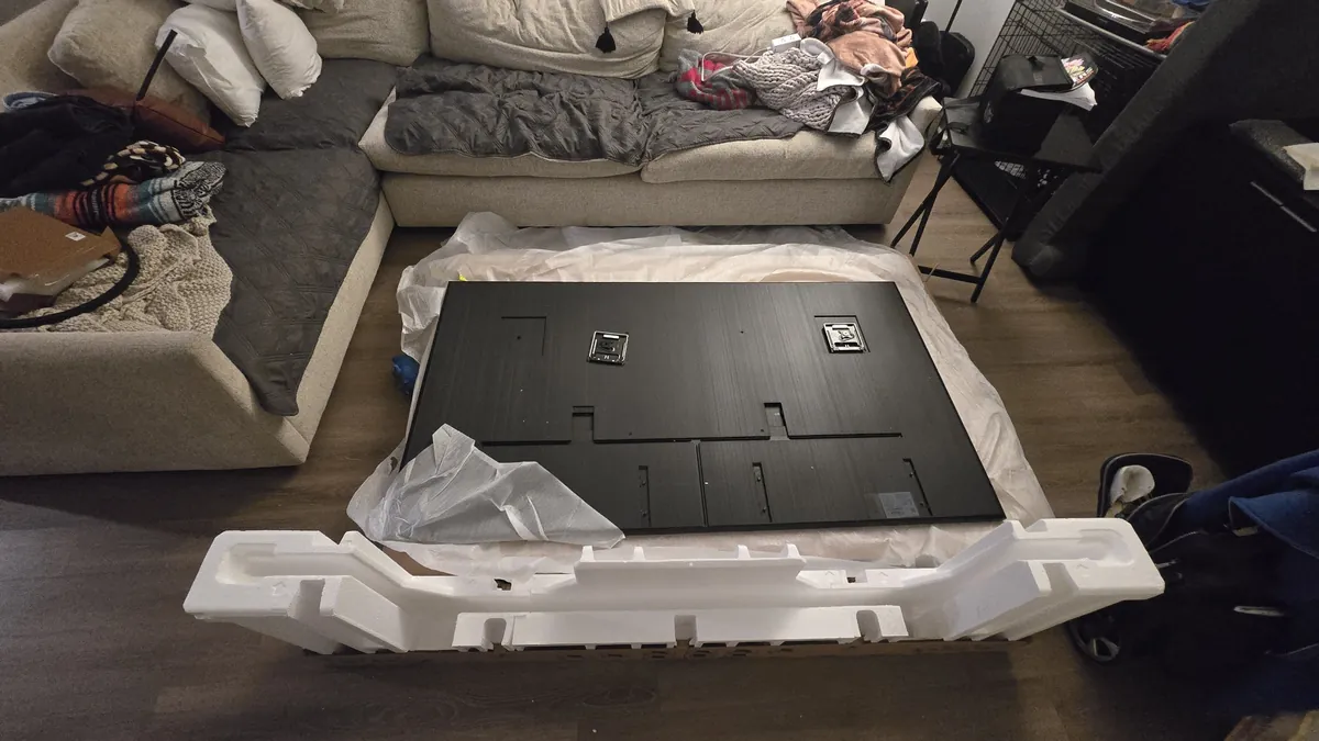 Samsung Frame TV lying screen-down on its box, with the mounting brackets on the back