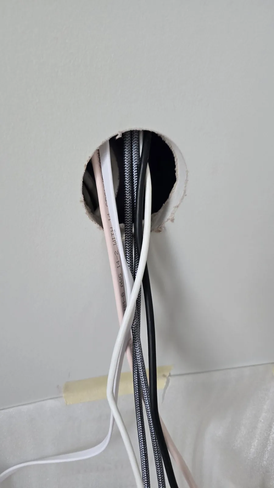 Several cables coming down out of a round hole in the wall