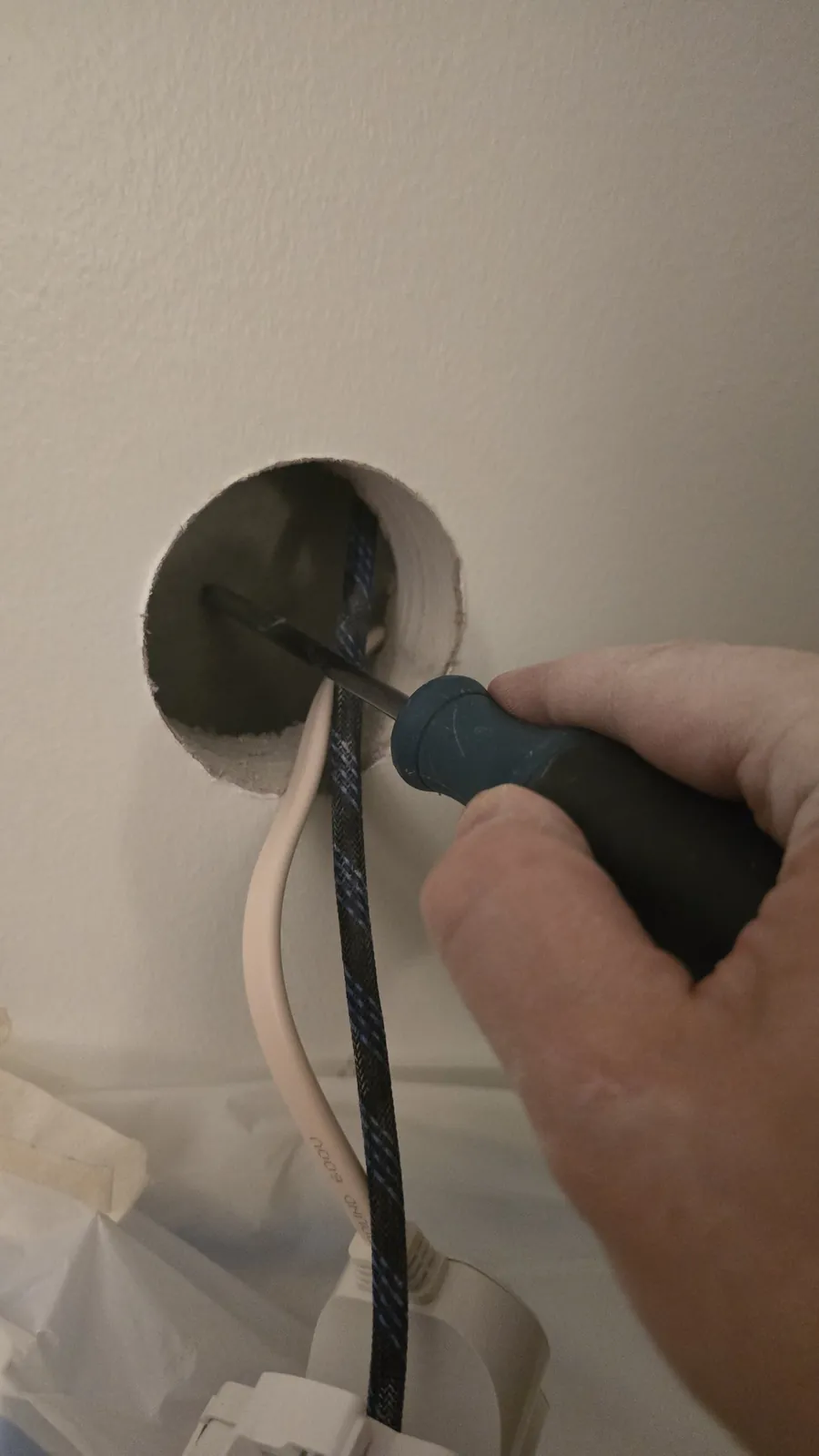 Screwdriver showing the shallow gap between drywall and concrete inside a round hole