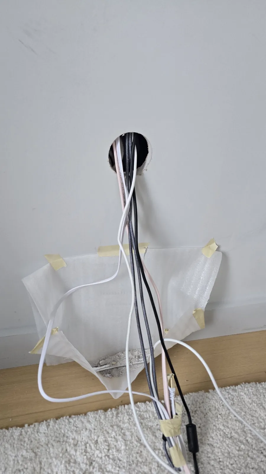 Cables coming out of the wall above a bag taped to the wall to catch dust