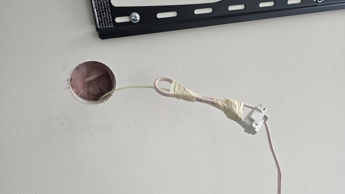 Power cable taped securely to the end of a fish tape coming out of a round hole
