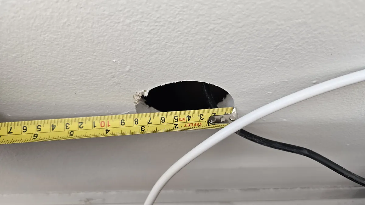 Round 3-inch hole cut in drywall, measured with a tape measure