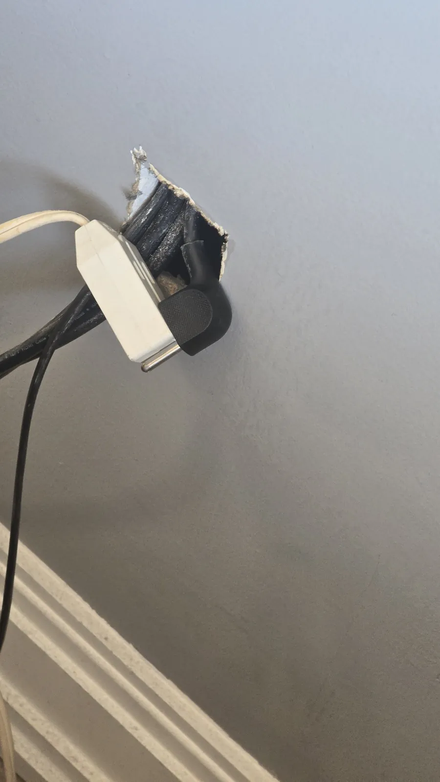 A regular black power cord pushed through a hole in the wall